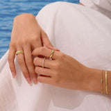 Close-up of hands with gold rings and bracelets against a blurred blue water background