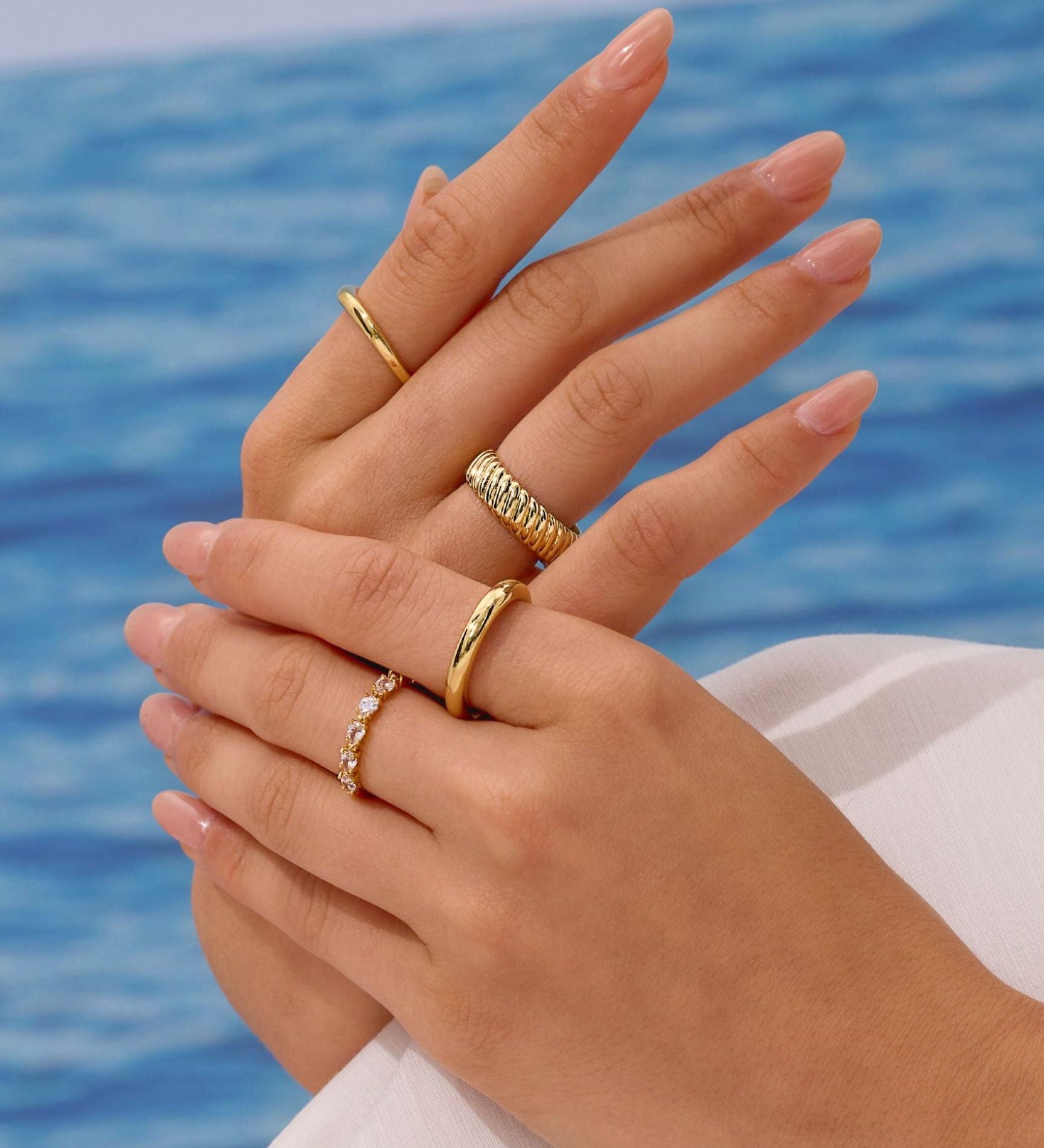 Close-up of hands with gold rings against a blue water background