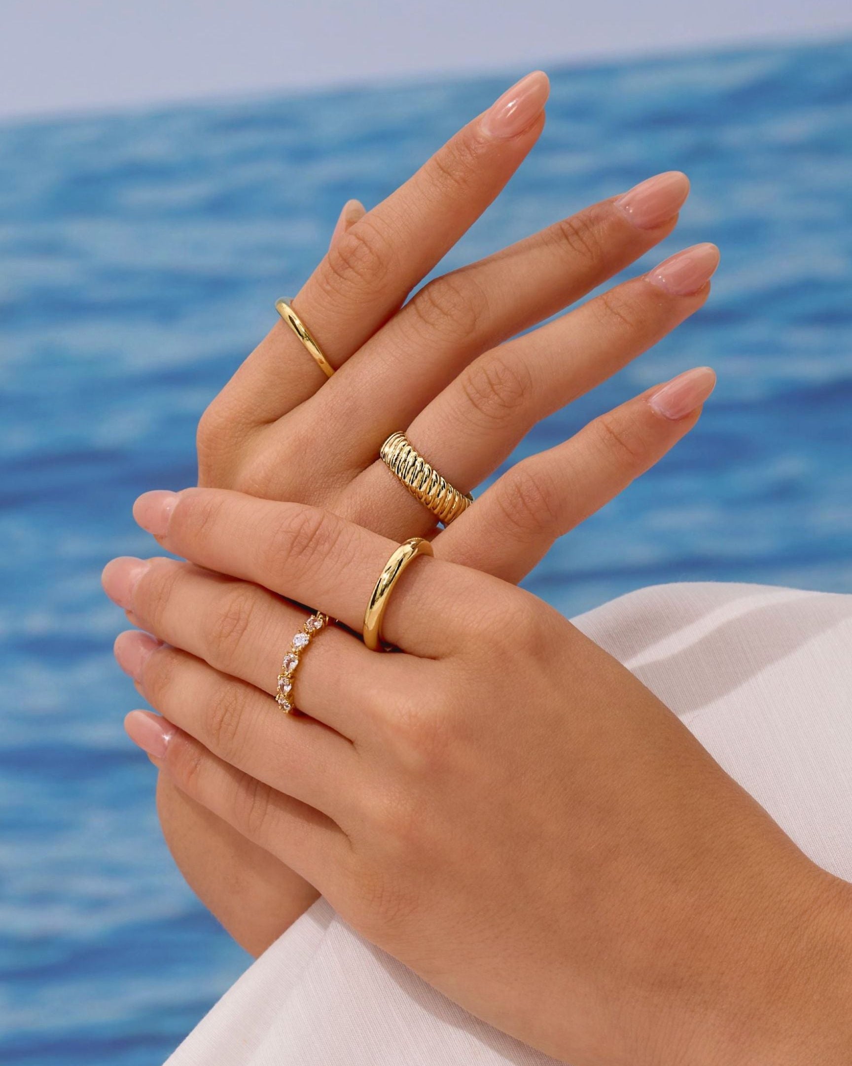 Close-up of hands with gold rings against a blue water background