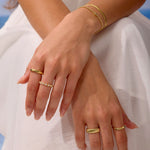 Close-up of hands wearing gold rings and bracelets on a light background