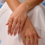 Close-up of hands wearing gold rings and bracelets on a light background