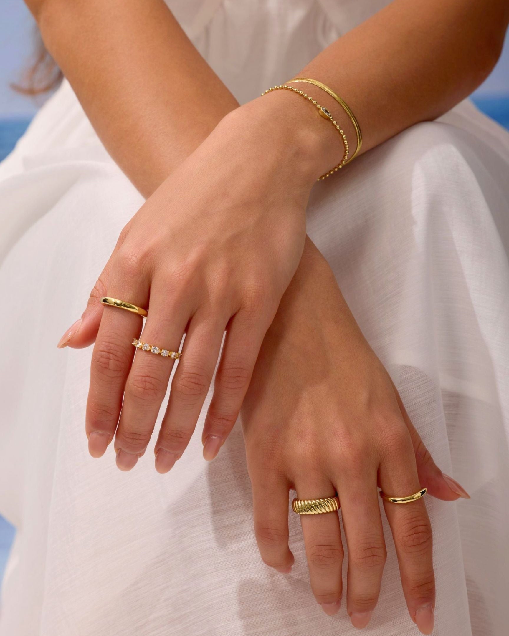 Close-up of hands wearing gold rings and bracelets on a light background