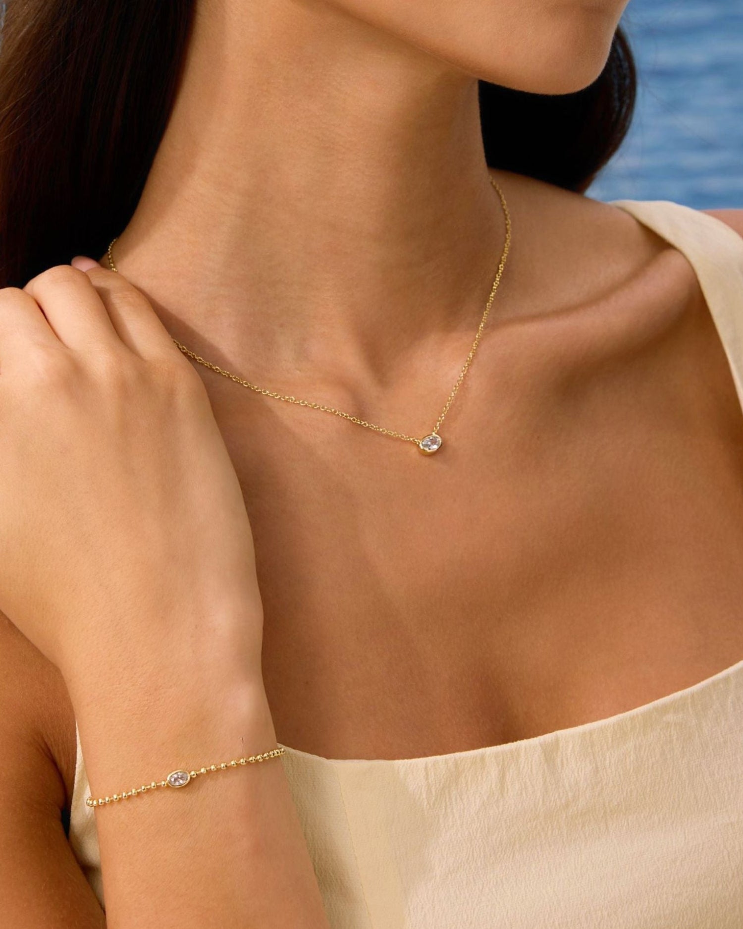 Woman wearing a gold necklace and bracelet with a blue ocean background