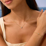 Woman wearing a gold necklace and bracelet with a blurred beach background