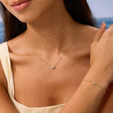 Woman wearing a gold necklace and bracelet with a blurred beach background