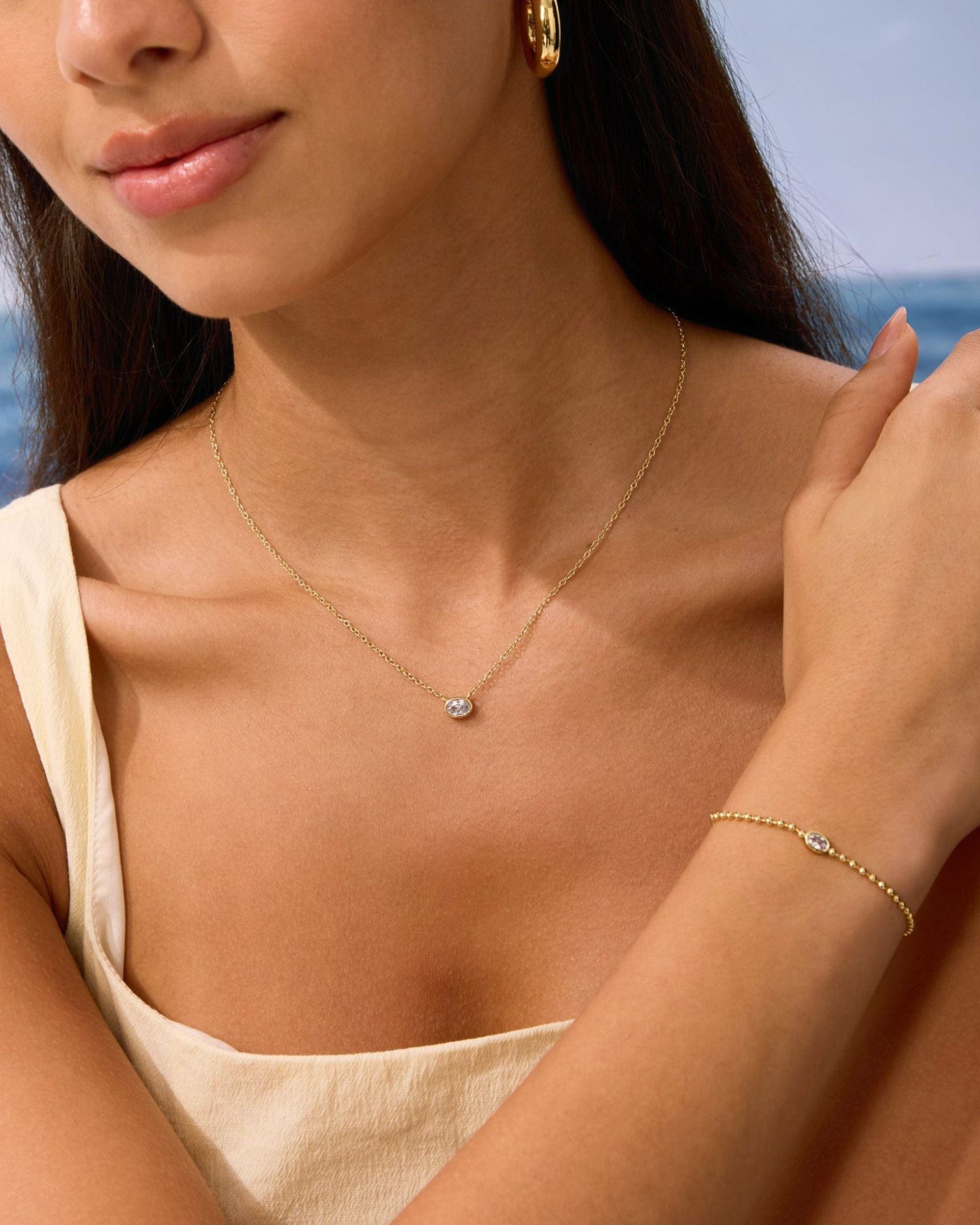 Woman wearing a gold necklace and bracelet with a blurred beach background