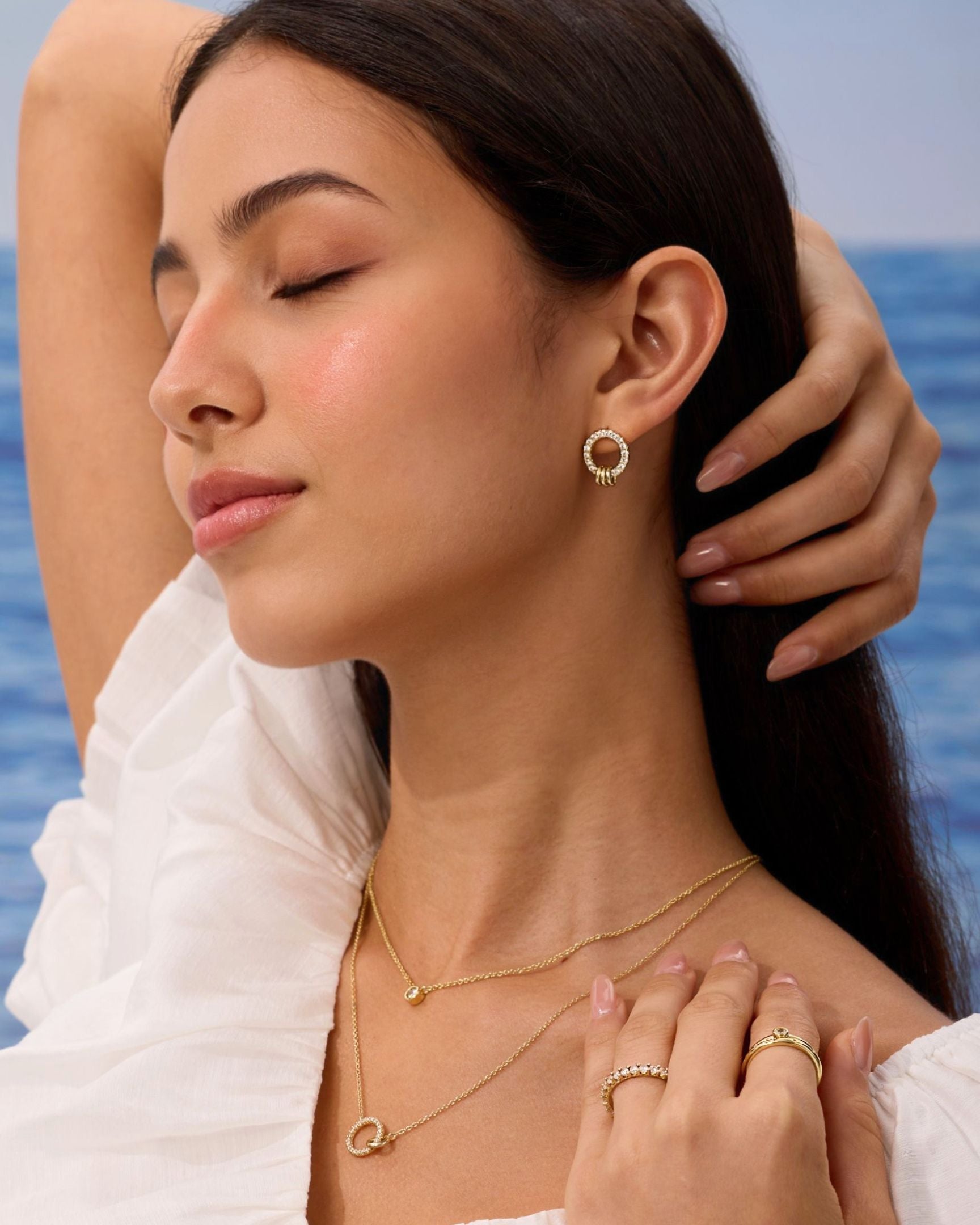 Woman wearing gold jewelry with a blurred ocean background