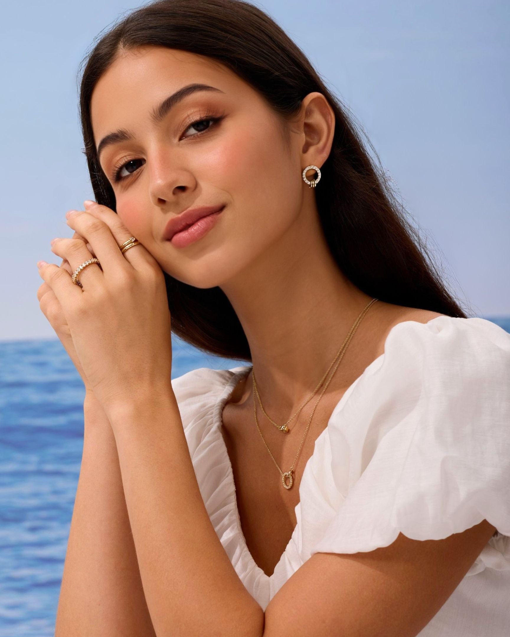 Woman wearing gold jewelry with a blue ocean background