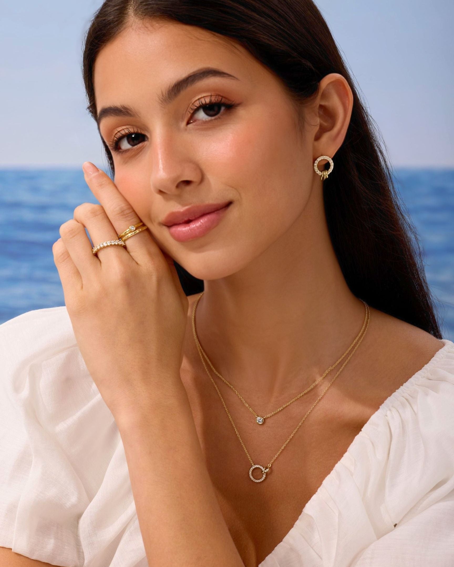 Woman wearing gold jewelry with a blue ocean background