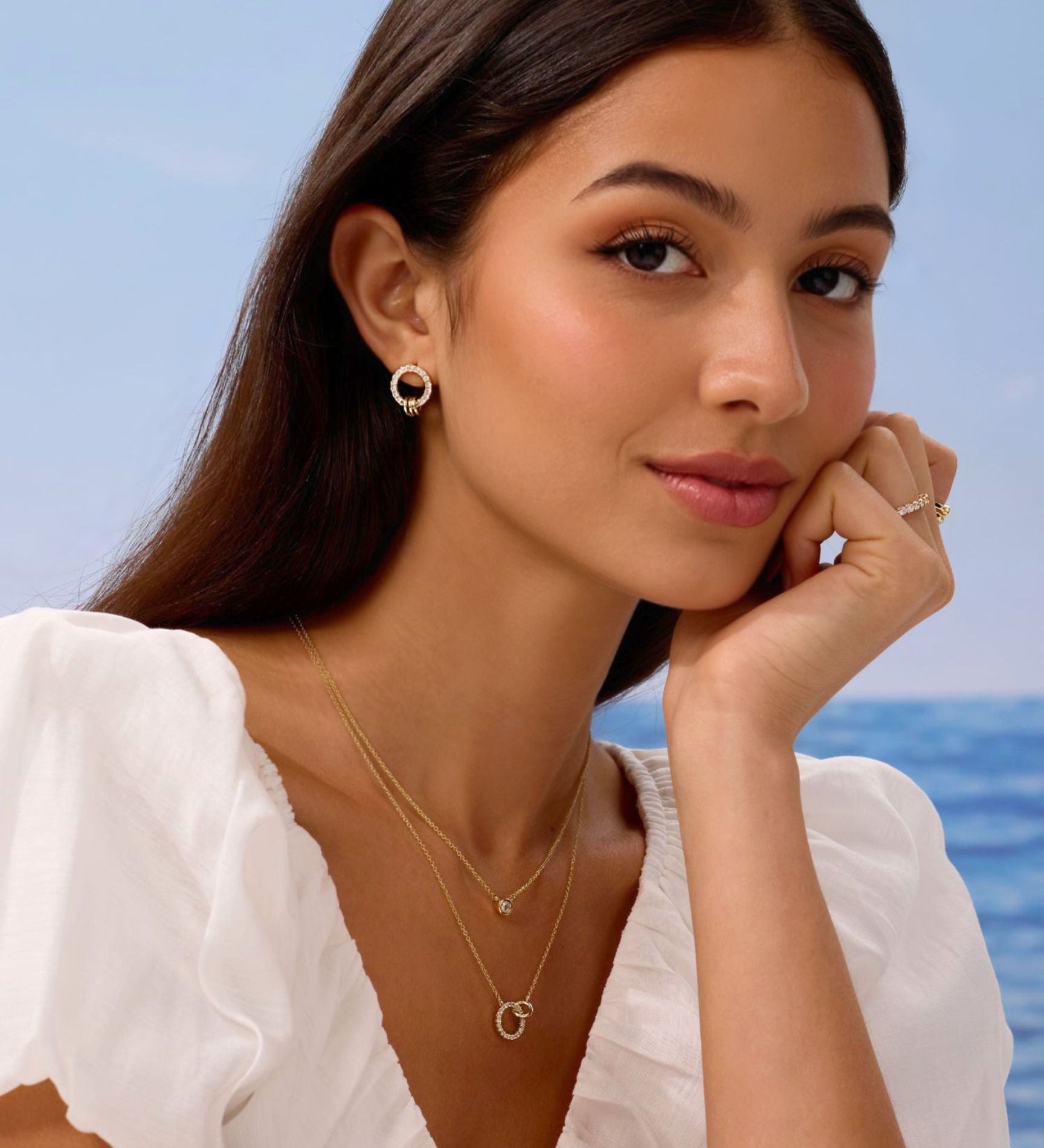 Woman wearing gold jewelry with a blurred ocean background