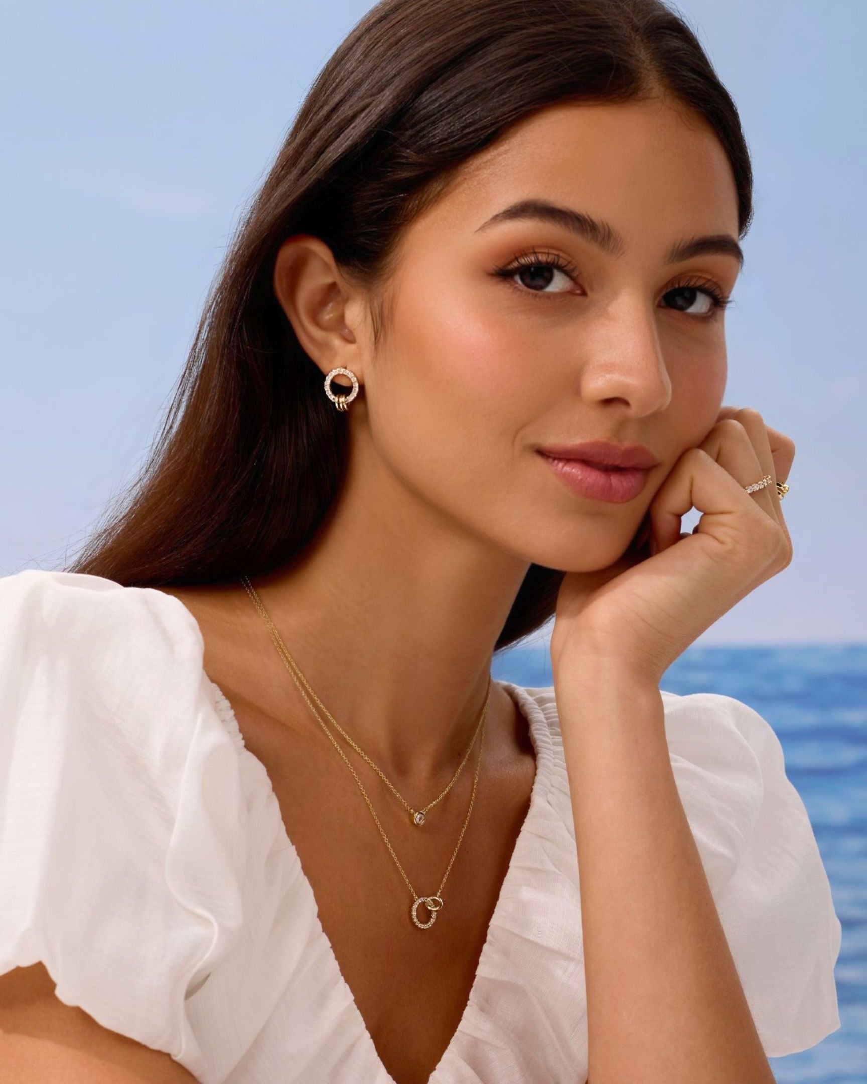 Woman wearing gold jewelry with a blurred ocean background