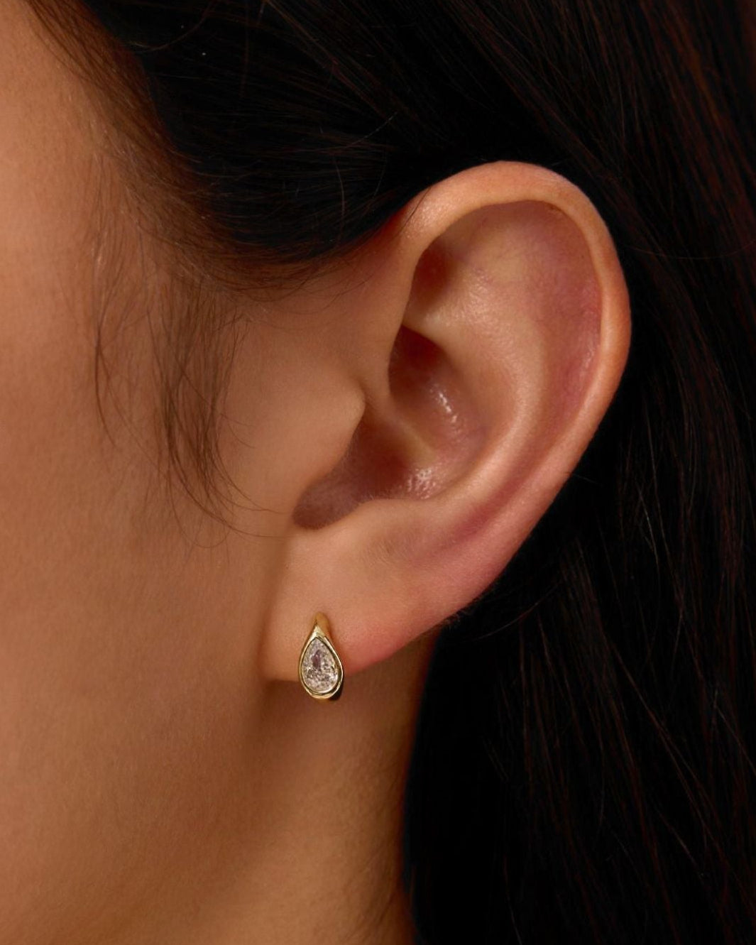 Close-up of a person wearing a teardrop-shaped earring with a blurred background