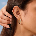 Close-up of a person wearing a gold hoop earring with a blurred background
