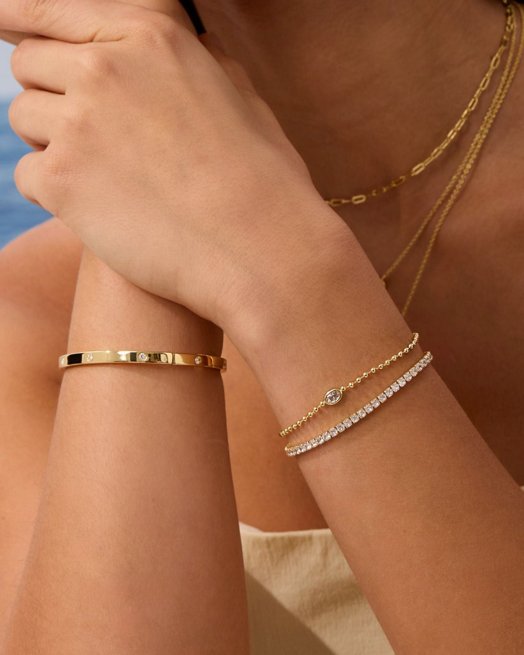 Close-up of a person's arm wearing gold bracelets with a blurred background