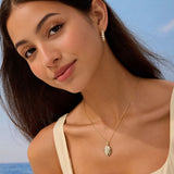 Woman wearing a necklace with a pendant against a blue sky and ocean background