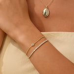 Gold necklace and bracelets on a person's wrist against a beige background
