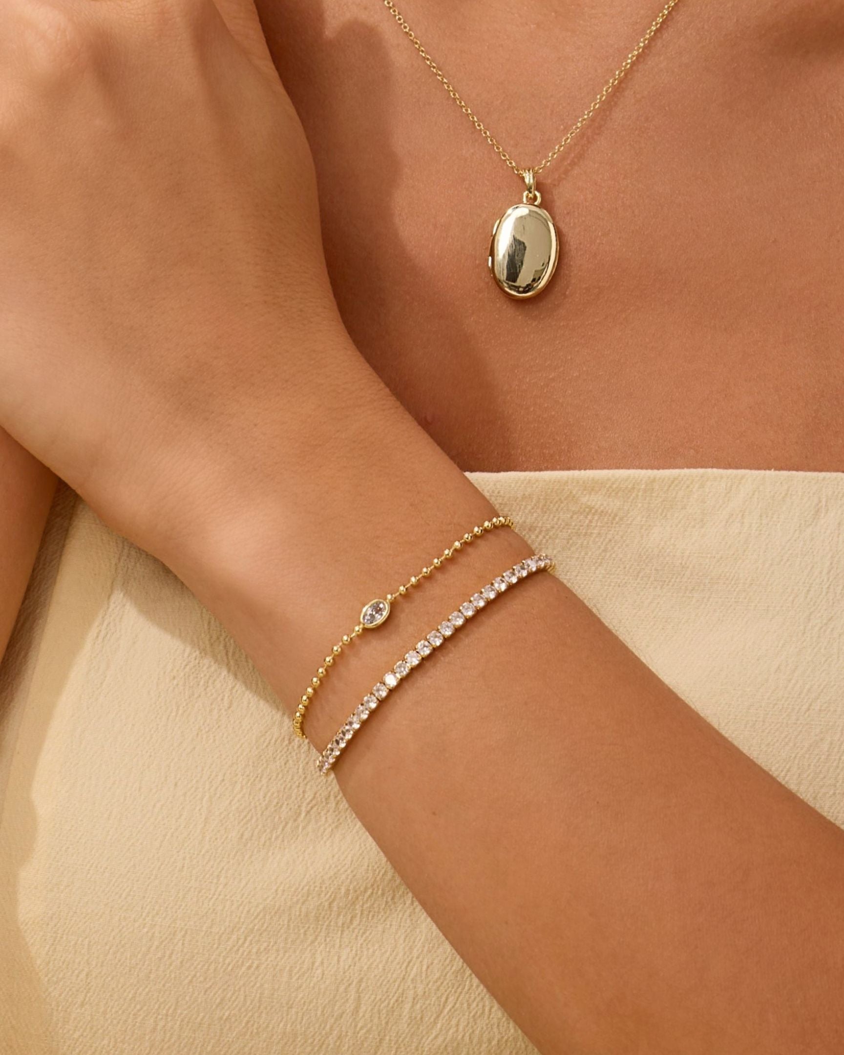 Gold necklace and bracelets on a person's wrist against a beige background