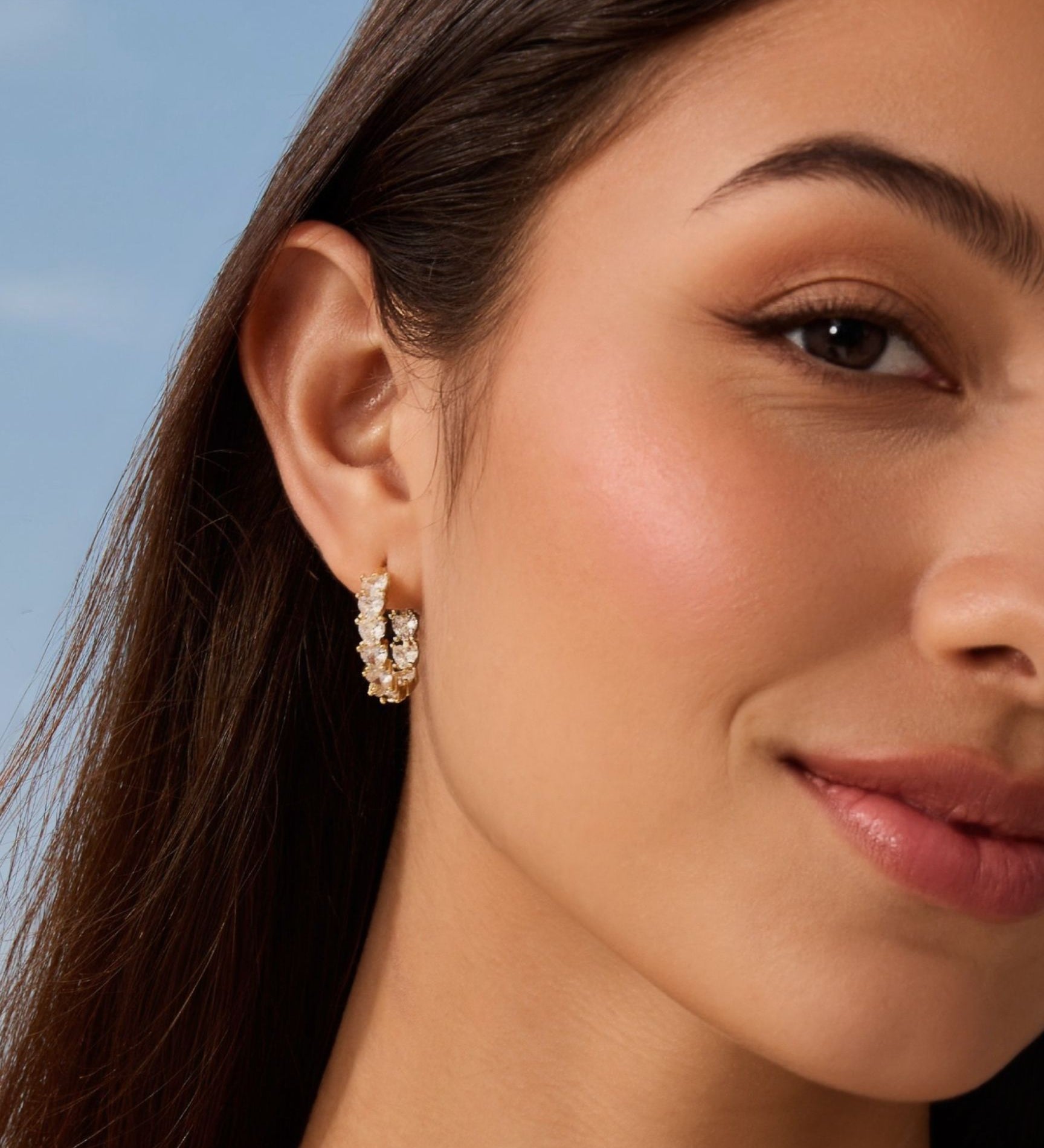 Close-up of a woman wearing diamond hoop earrings with a clear blue sky background