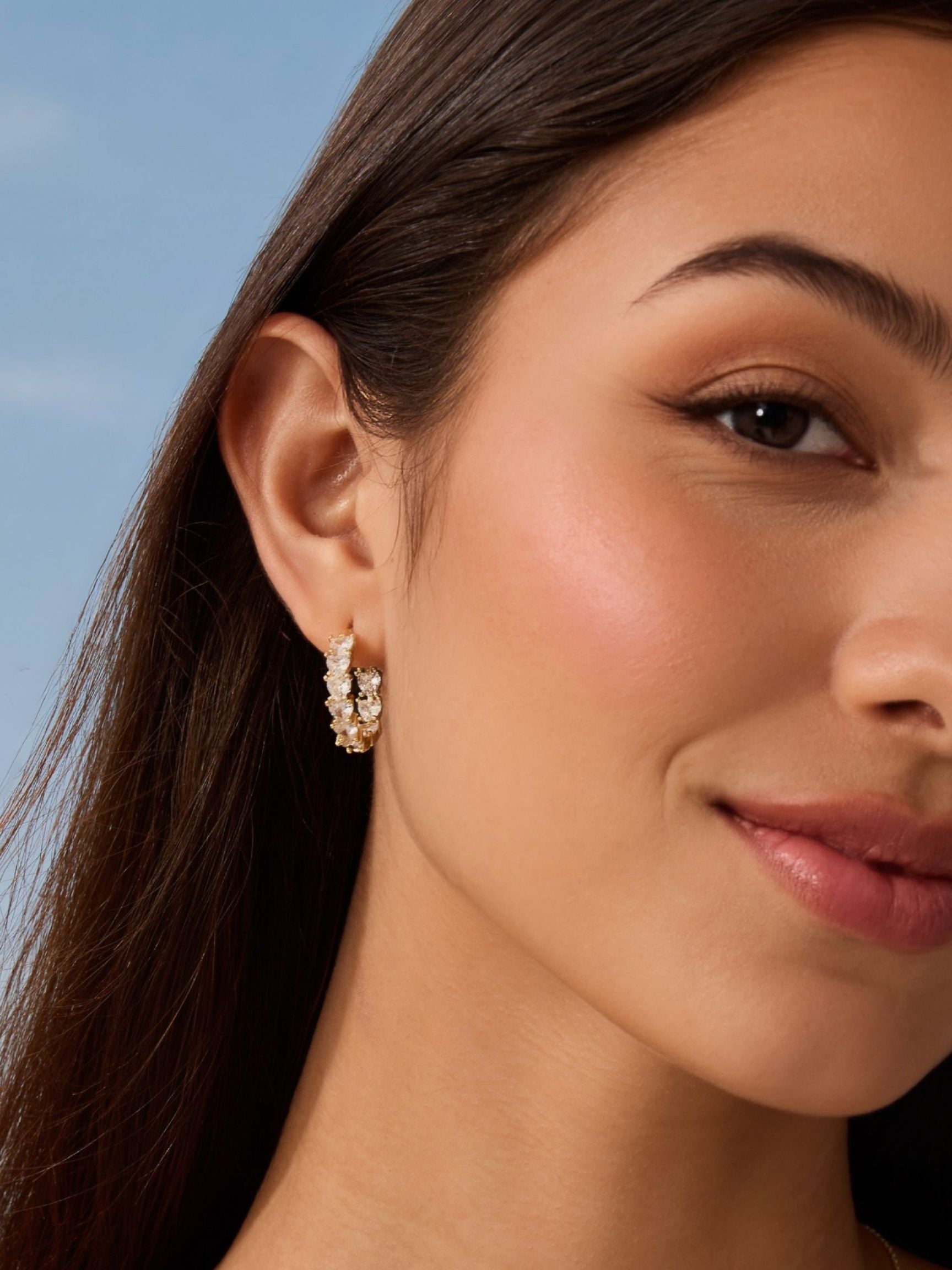 Close-up of a woman wearing diamond hoop earrings with a clear blue sky background