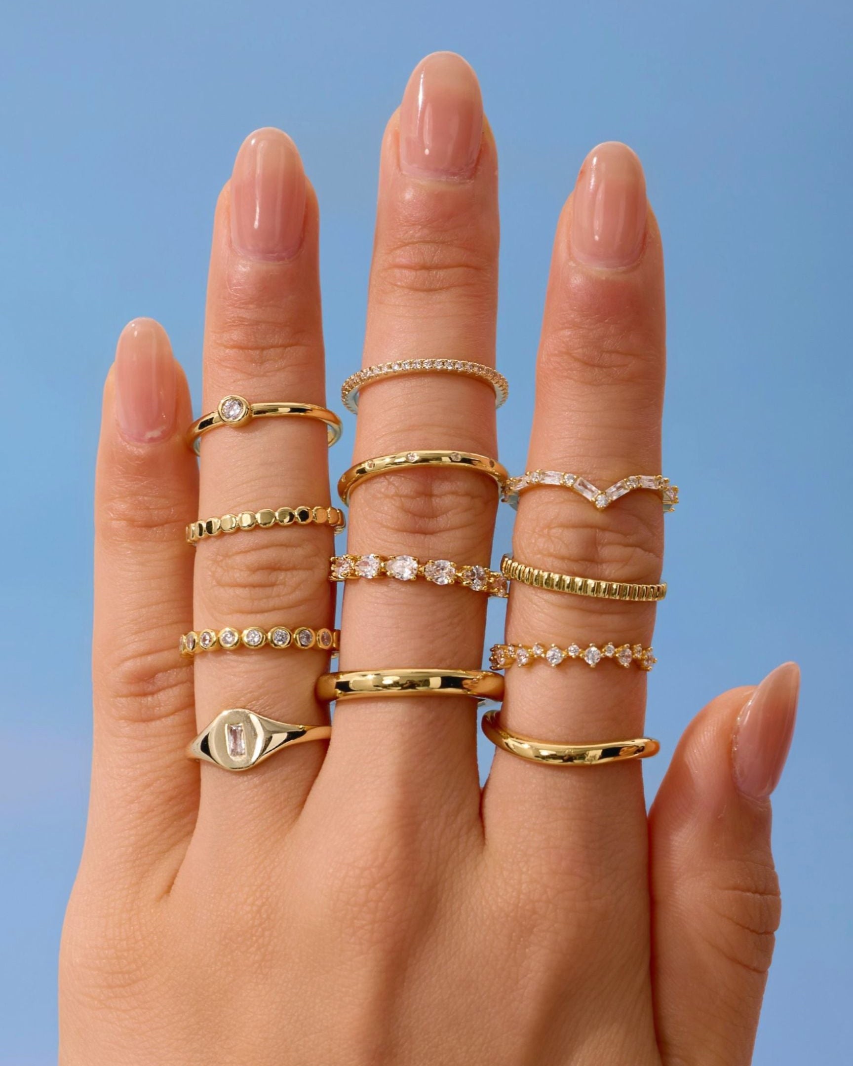 Hand wearing multiple gold rings with a blue background